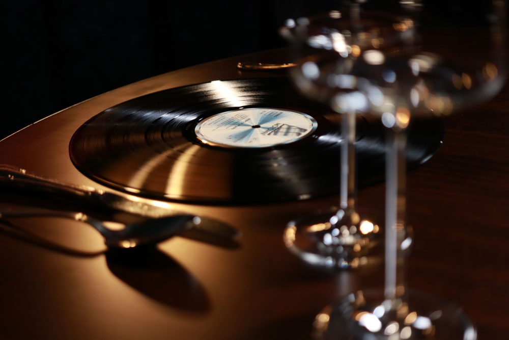 Weingläser im Vordergrund und Schallplatte mit Besteck im Hintergrund