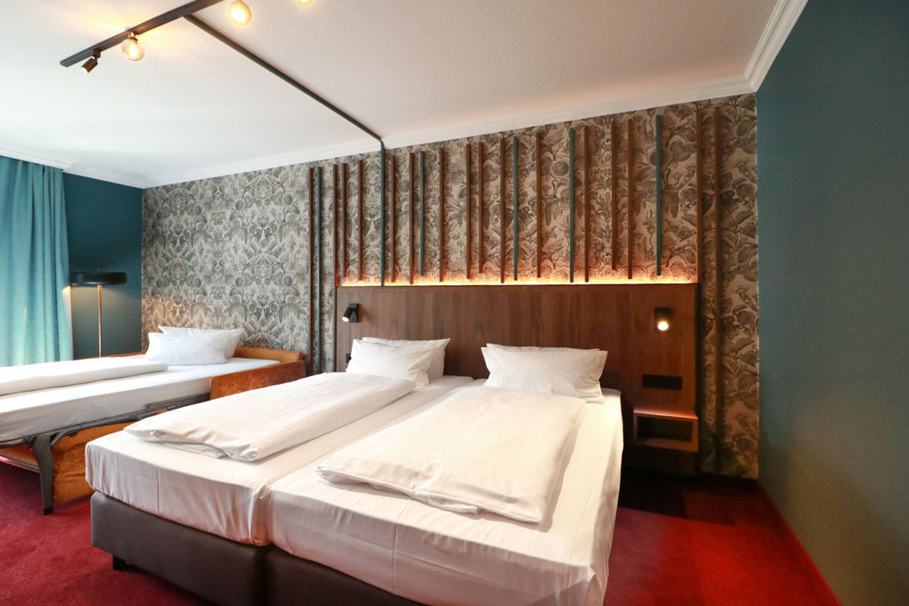 Helles geräumiges Hotelzimmer mit aufgeklapptem Schlafsofa sowie Doppelbett