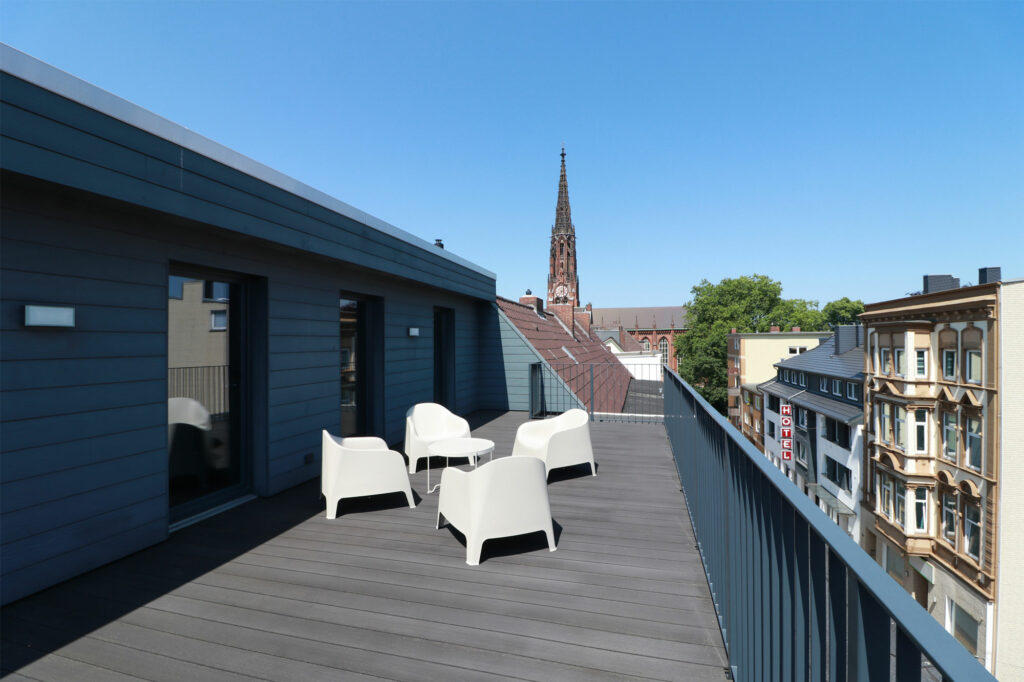 Dachterrasse im Penthouse mit Sitzmöbeln und Tisch bei Tageslicht mit Blick auf einen Kirchturm