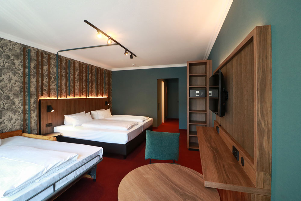 Geräumiges helles Zimmer mit Tisch, Stuhl, TV sowie Doppelbett und aufgeklapptes Schlafsofa