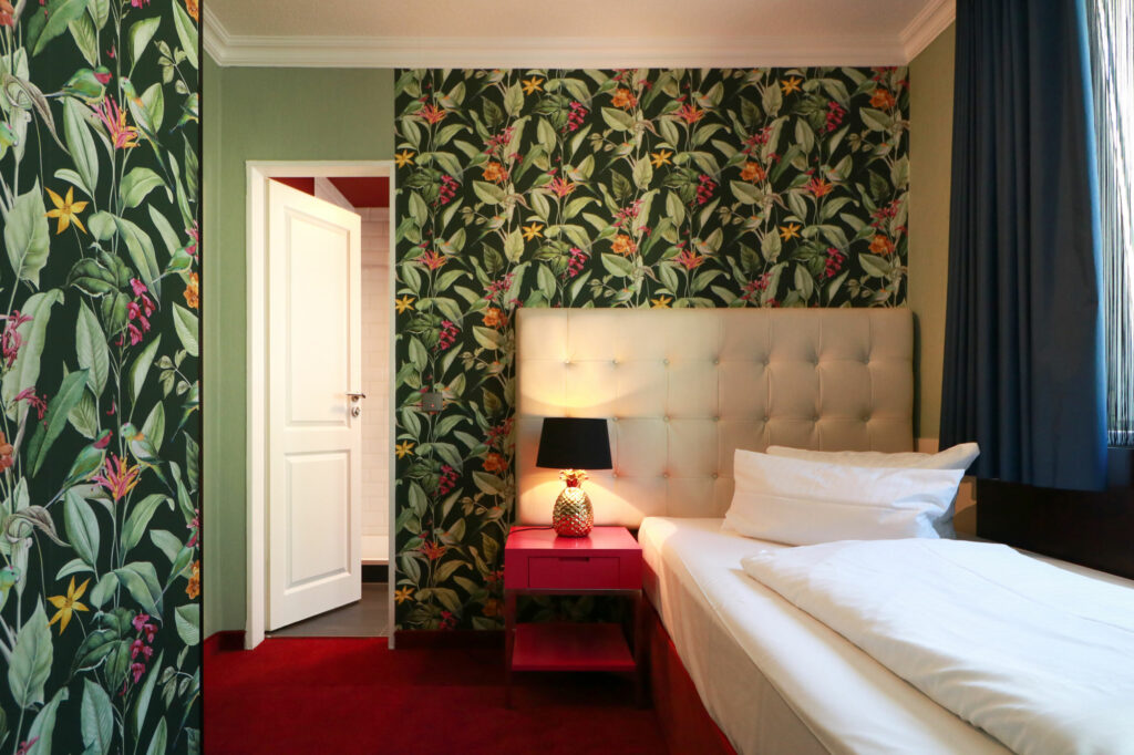 Zimmer bei Tageslicht mit floraler Tapete und Einzelbett