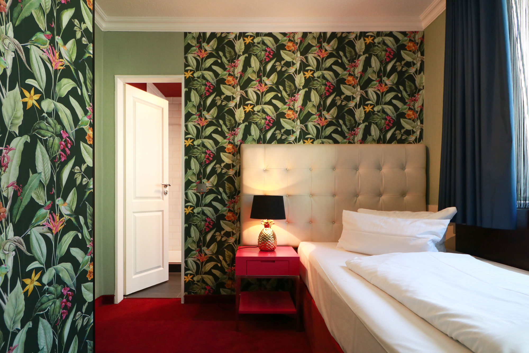Zimmer bei Tageslicht mit floraler Tapete und Einzelbett