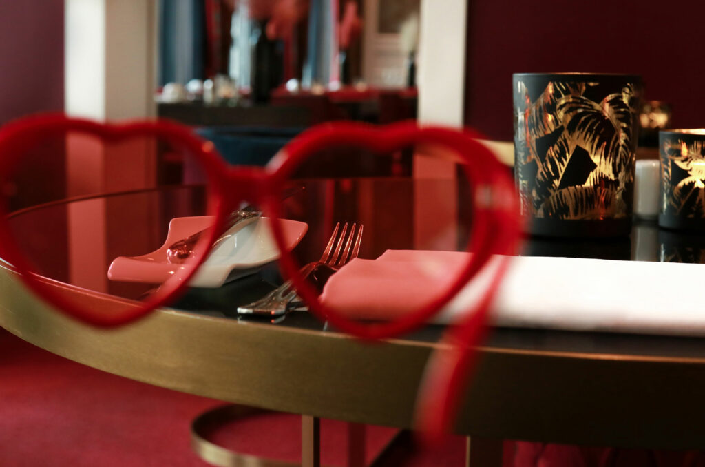Rote Herzbrille, durch die man Besteck in einem hellen Restaurant sehen kann